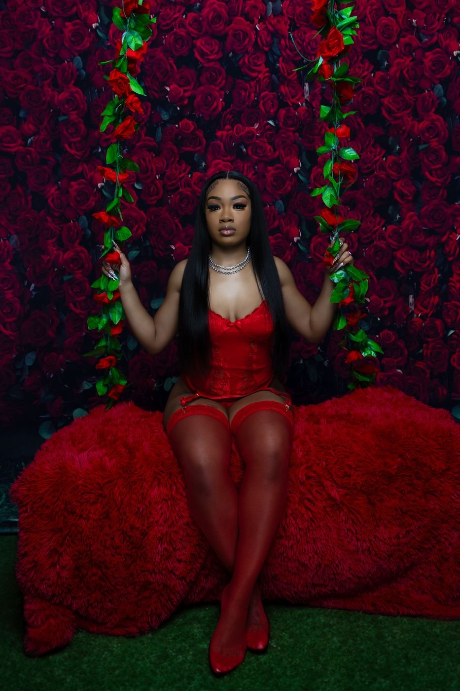 Woman on a flower swing in front of a red rose wall, styled studio portrait