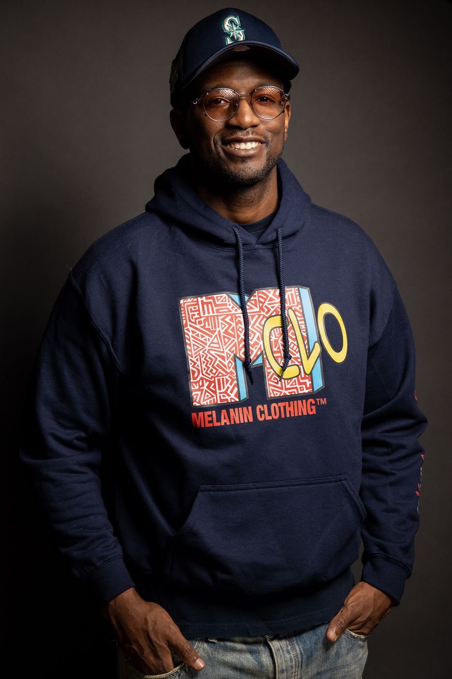 Smiling model in a navy Melanin Clothing graphic hoodie, studio portrait