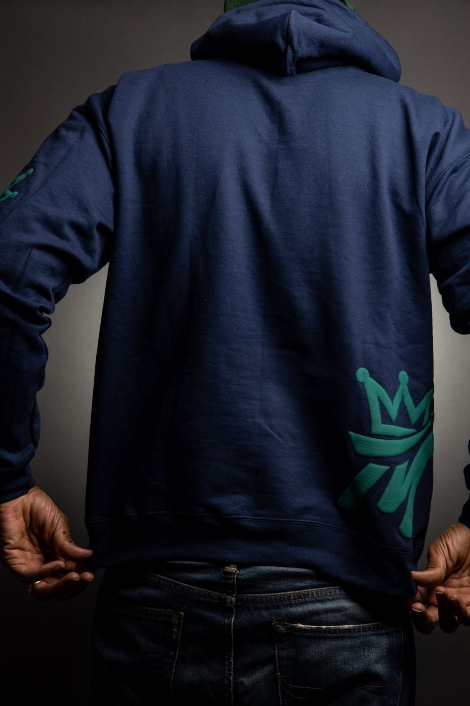 Model from behind in a navy Melanin CLO hoodie with green crown sleeve print, studio
