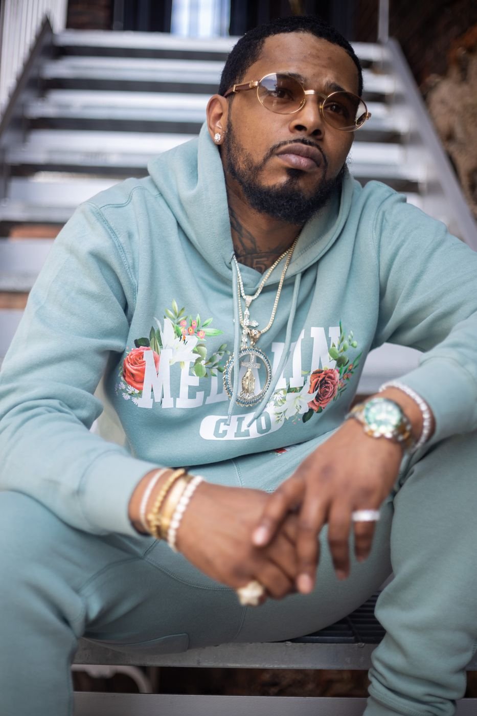 Model seated on stairs in a sage Melanin CLO tracksuit