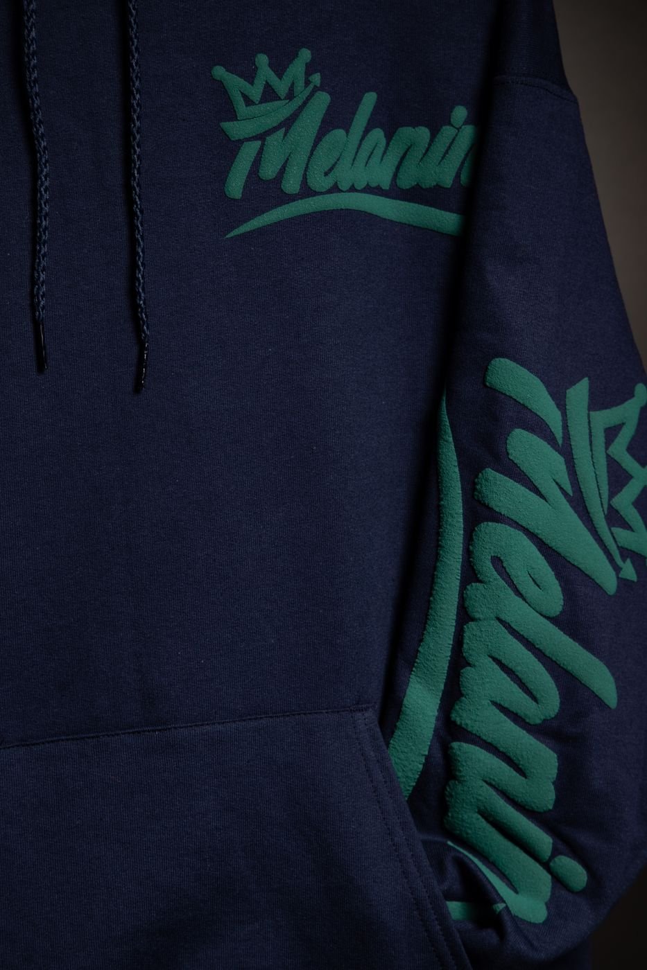 Detail of the green Melanin script print on a navy hoodie sleeve