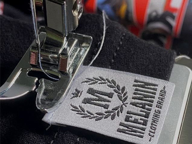 Melanin Clothing Brand woven label being stitched on a sewing machine