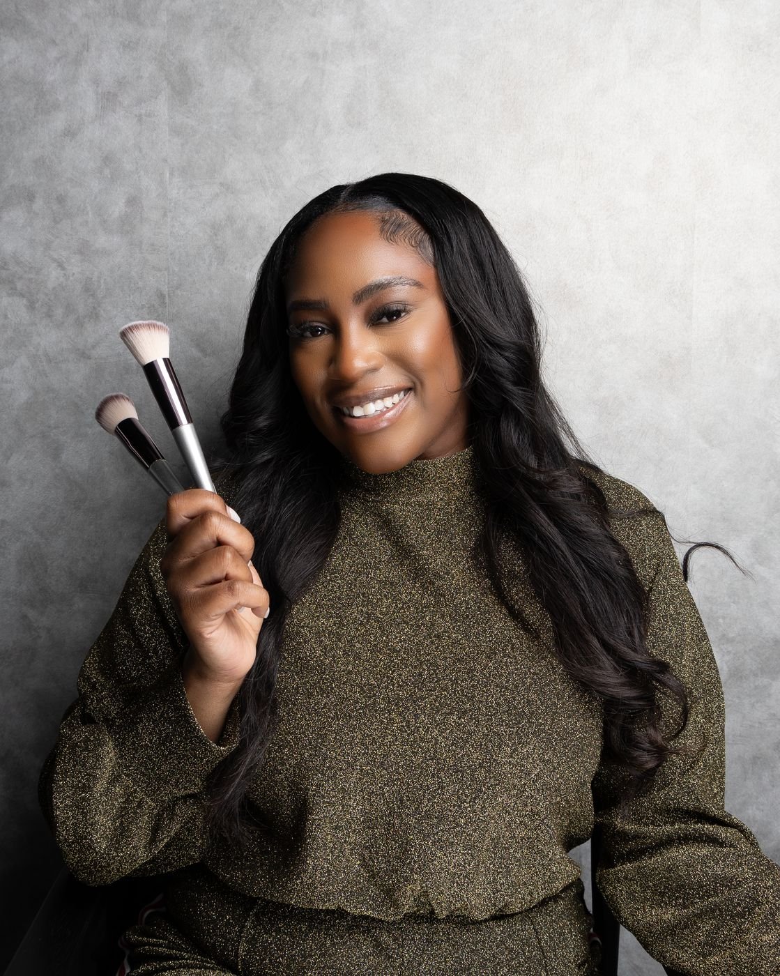 Smiling beauty professional holding makeup brushes, grey backdrop headshot